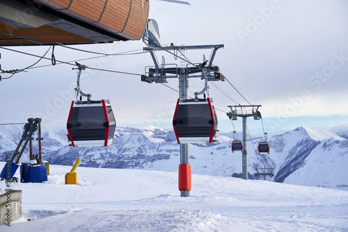 Cable car gondola at ski resort with snowy mountains on background. Modern ski lift with funitels and supporting towers high in the mountains on winter day. No people. photo