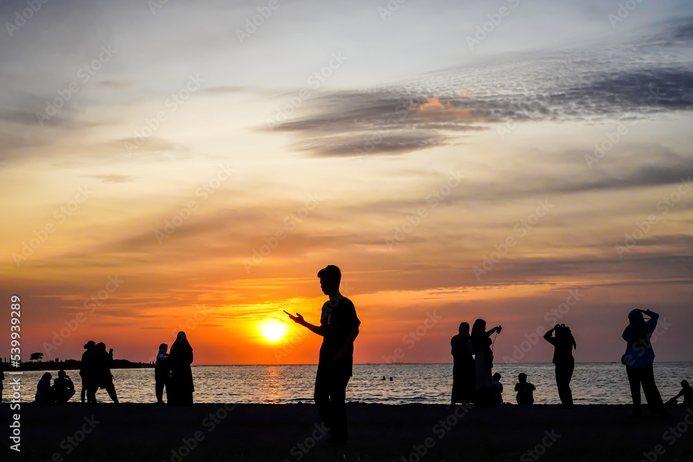 Silhouettes of people taking pictures on the beach with a sunset background