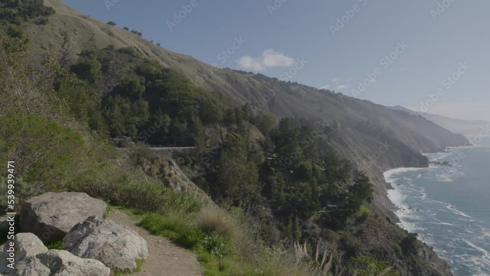 Panning shot from mountain side to the Pacific ocean at Big Sur California beach with waves crashing on a rocky shore Panning shot from mountain side to the Pacific ocean at Big Sur California beach with waves crashing on a rocky shore