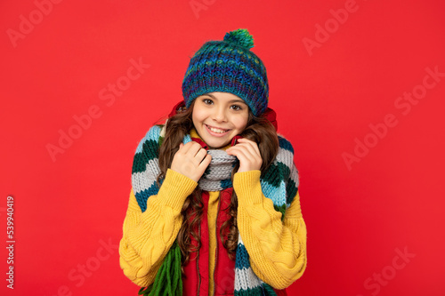 cheerful teen girl in knitted winter hat and scarf on red background, keep warm