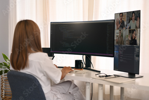 Rear view of female developer having video conference and working with coded data on computer screen