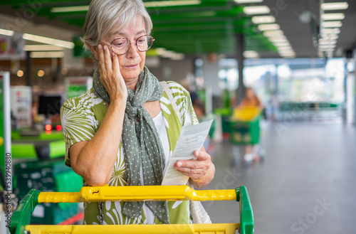 Принти на полотні Senior woman in the supermarket checks her grocery receipt looking worried about