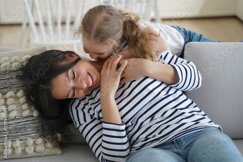 Obraz na plátně Happy little daughter tickling laughing mom or babysitter, sitting on couch, hav