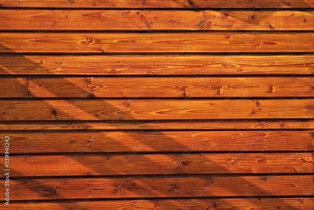 background or texture for your site or product. photograph of a wooden wall made of planed clapboard in the rays of bright sunlight. background or texture for your site or product. photograph of a wooden wall made of planed clapboard in the rays of bright sunlight.