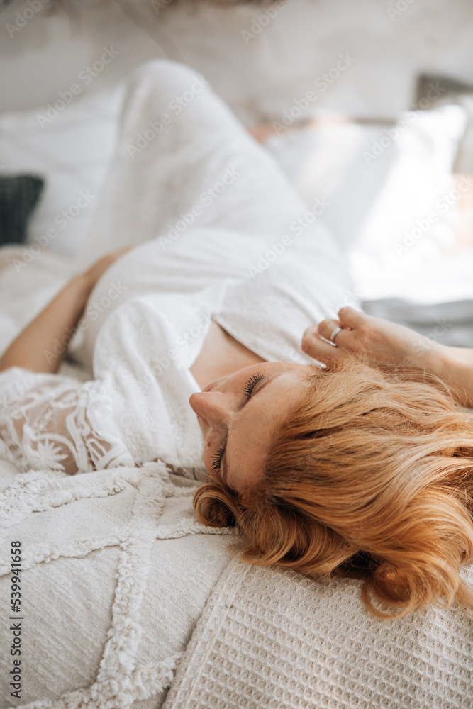 European pregnant woman relaxing on sofa at home. Pregnant redhead female peacefully lying on comfortable bed at home. European pregnant woman relaxing on sofa at home. Pregnant redhead female peacefully lying on comfortable bed at home.