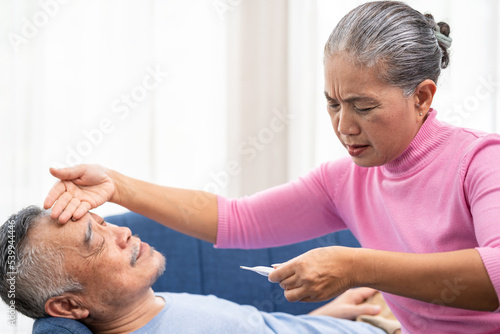 Elderly woman checking temperature on her husband's forehead. Worried senior woman and sick man