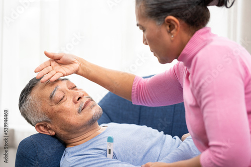 Elderly woman checking temperature on her husband's forehead. Worried senior woman and sick man