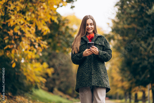 Beautiful woman walking in autumn park and using phone
