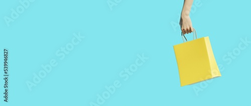 Yellow shopping bag on blue background hold by hand. 3d rendering