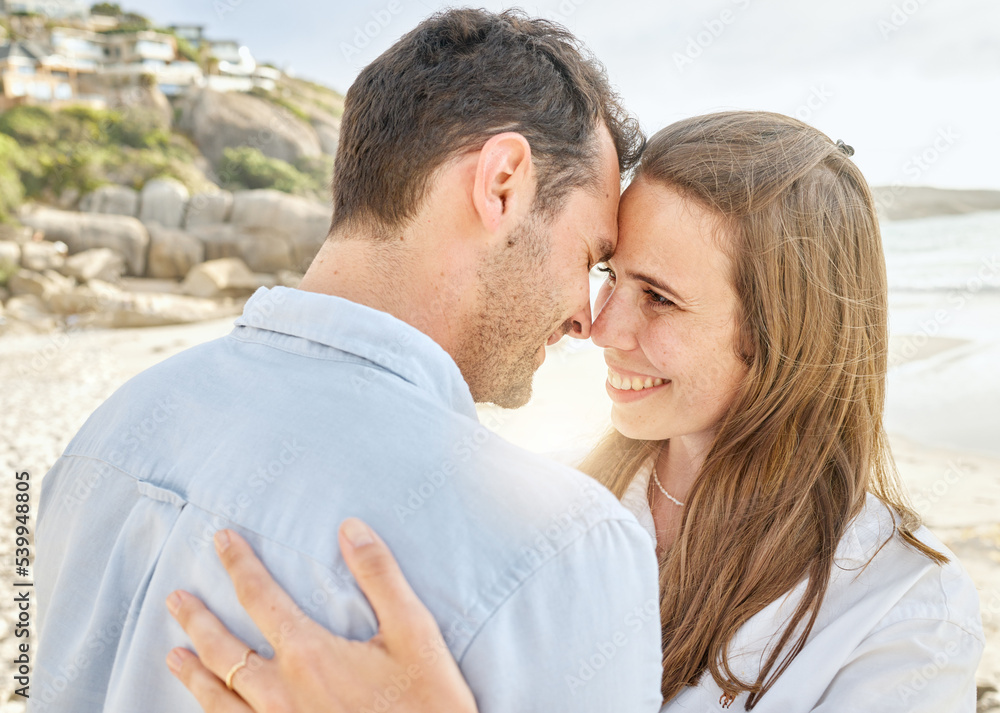 Couple, love and hug on a beach together for an engagement honeymoon or anniversary by the sea. Young man and woman smile feeling happy and romantic by the ocean water and sand with happiness
