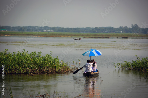 School children rowing boat to cross the river and attend school. School students holding colorful umbrellas in a boat in the middle of the river.