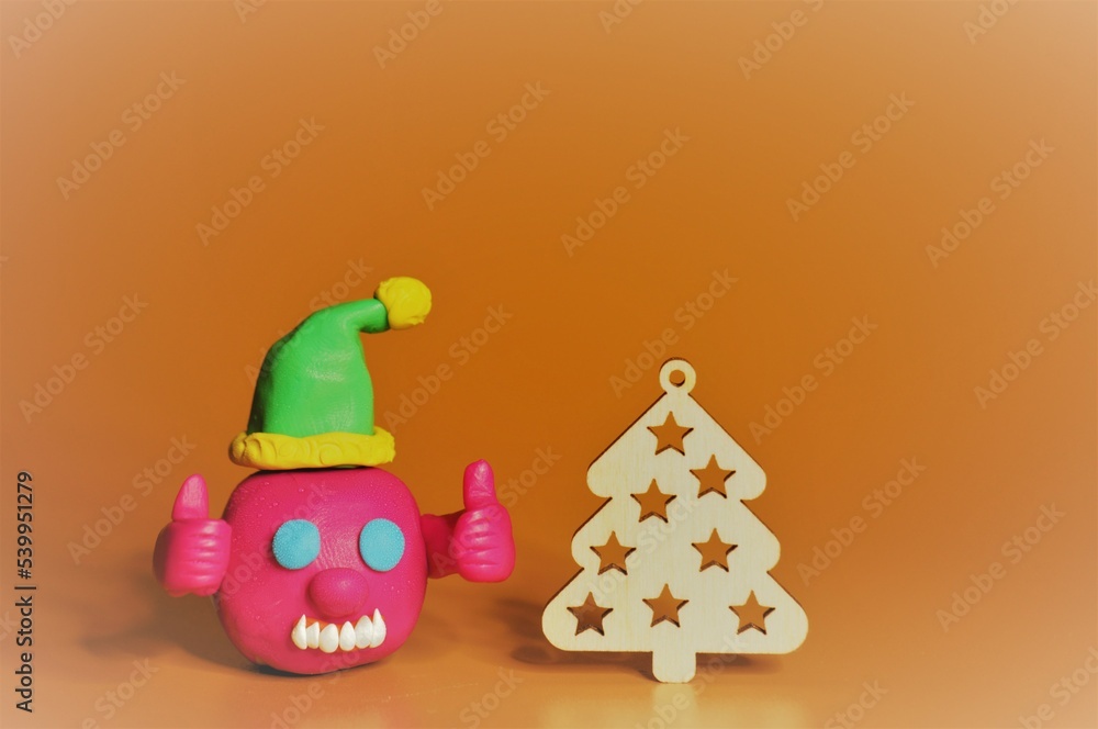 Fototapeta premium A figure of a joyful virus in a festive hat. There is a Christmas tree nearby. A festive event.