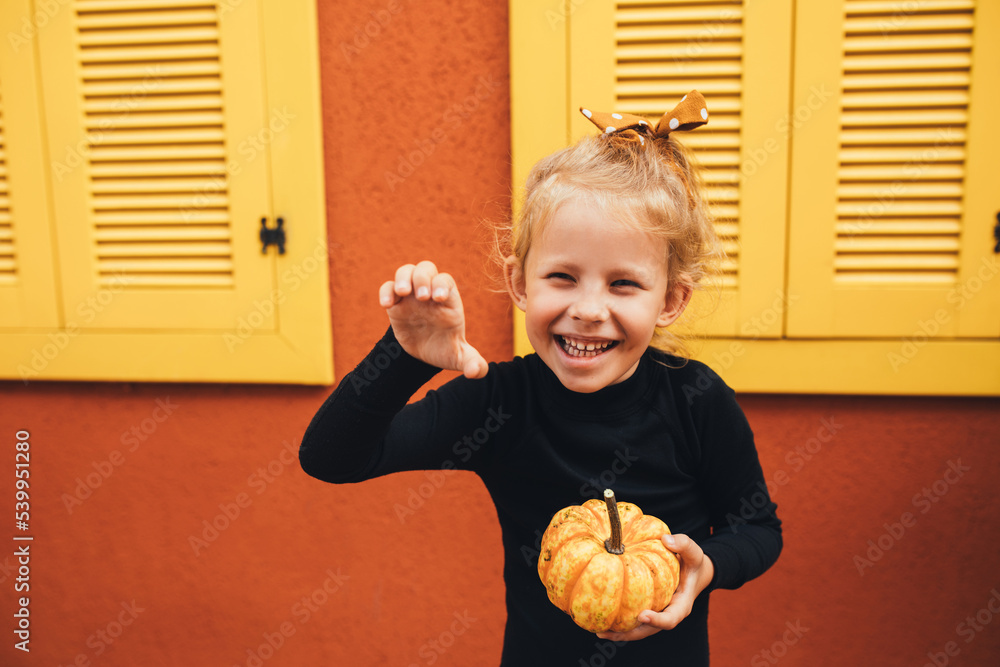 Fototapeta premium Cute little girl holding small pumpkin on the orange background.