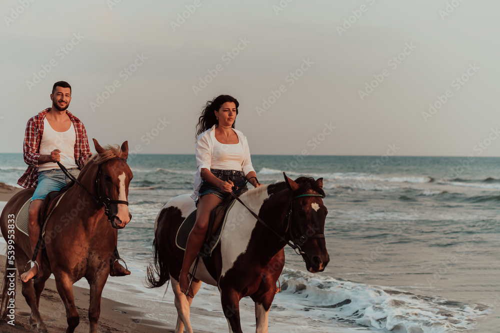 A loving couple in summer clothes riding a horse on a sandy beach at sunset. Sea and sunset in the background. Selective focus A loving couple in summer clothes riding a horse on a sandy beach at sunset. Sea and sunset in the background. Selective focus