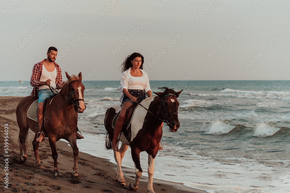 A loving couple in summer clothes riding a horse on a sandy beach at sunset. Sea and sunset in the background. Selective focus A loving couple in summer clothes riding a horse on a sandy beach at sunset. Sea and sunset in the background. Selective focus