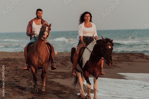 A loving couple in summer clothes riding a horse on a sandy beach at sunset. Sea and sunset in the background. Selective focus 