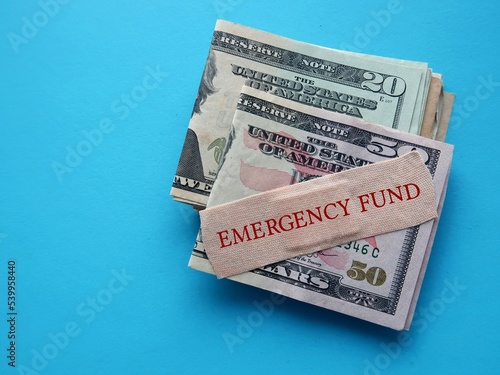 Cash dollar money on blue background with band aid written EMERGENCY FUND - smart financial planning to save money for contingency fund - for rainy day, future crisis, medical expenses or distress