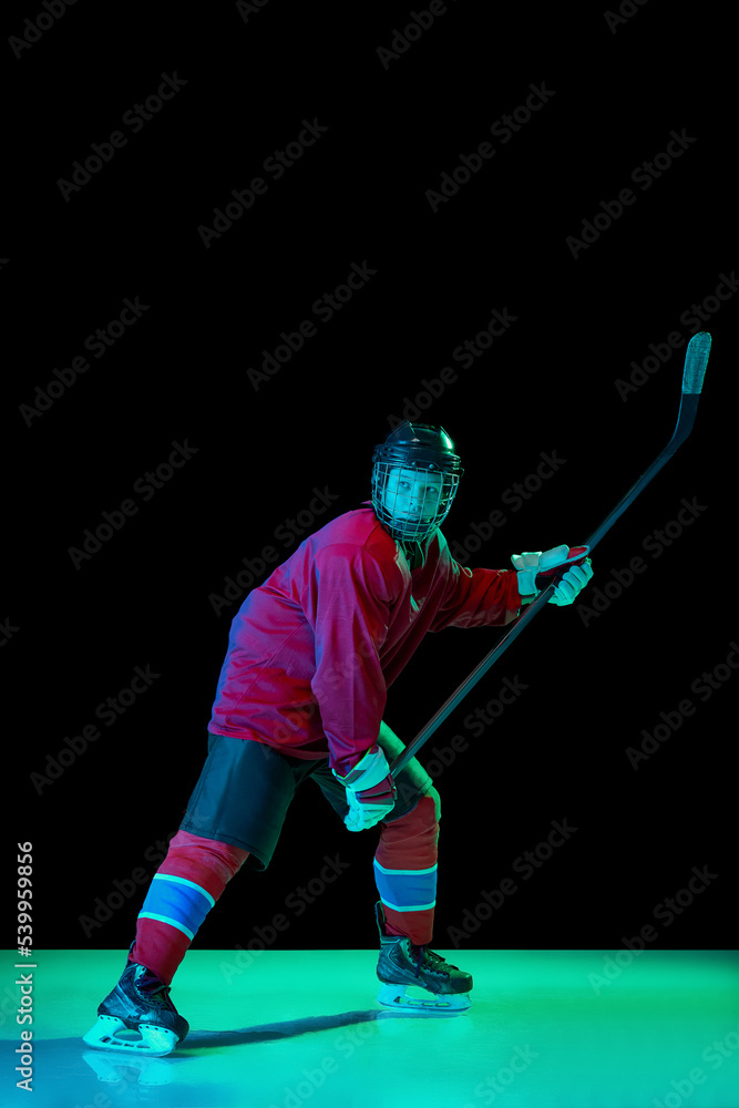 Powerful throw. Male ice hockey player in sports protective uniform in action over dark background in neon light. Sport, power, challenges, achievement, goals