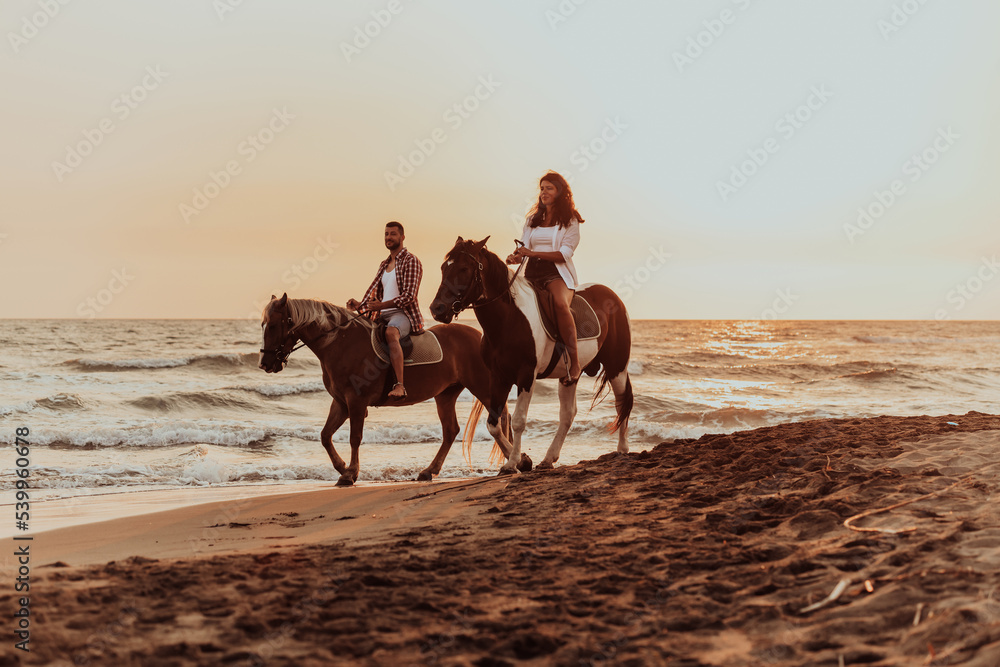 A loving couple in summer clothes riding a horse on a sandy beach at sunset. Sea and sunset in the background. Selective focus A loving couple in summer clothes riding a horse on a sandy beach at sunset. Sea and sunset in the background. Selective focus