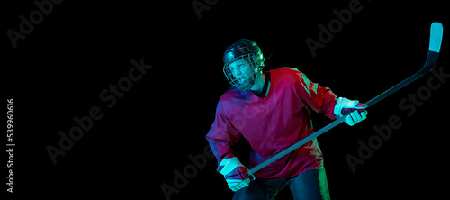 Training of male ice hockey player wearing hockey jersey, uniform and sports helmet in motion isolated over dark background in neon light © master1305