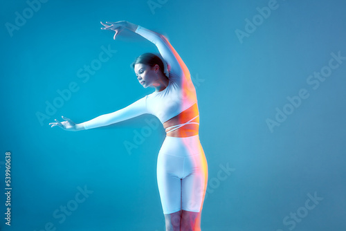 Fototapeta Naklejka Na Ścianę i Meble -  A elegant athletic girl does bends. Isolated figures of a fitness model in a white sports uniform on a blue background.