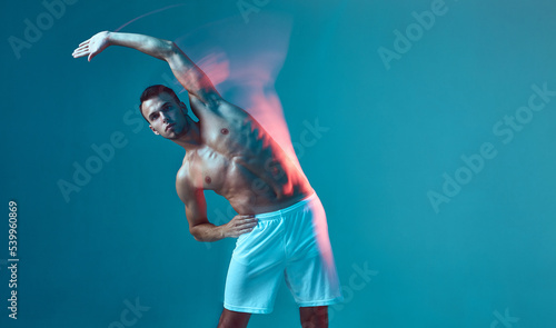 Fototapeta Naklejka Na Ścianę i Meble -  A handsome, athletic, pumped-up man leans to the left. A young man with a bare torso and white shorts on a blue background.