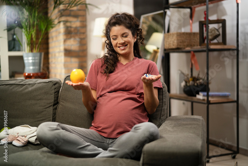 Pregnant woman choosing between pills and fruit.