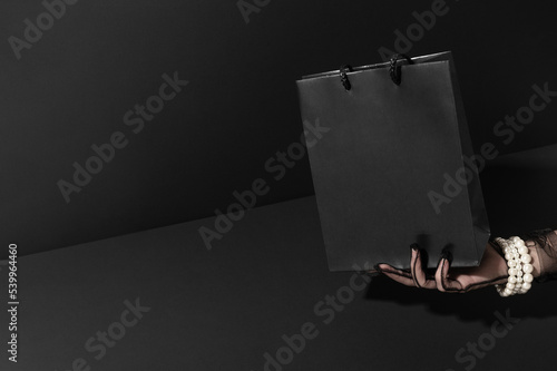 Empty shopping bag in elegant woman hand in dark studio closeup. Sales of expensive fashion products. Black Friday discounts for buyers (ID: 539964460)