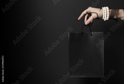 Lady with pearl bracelet presents blank shopping bag in dark studio closeup. Luxury goods for lower prices during Black Friday sales (ID: 539964472)