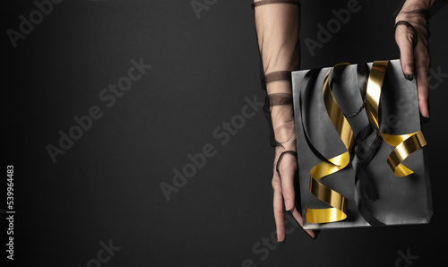 Woman with chiffon gloves demonstrates shopping bag with streamers in studio closeup. Black Friday sales preparation. Fashion industry (ID: 539964483)