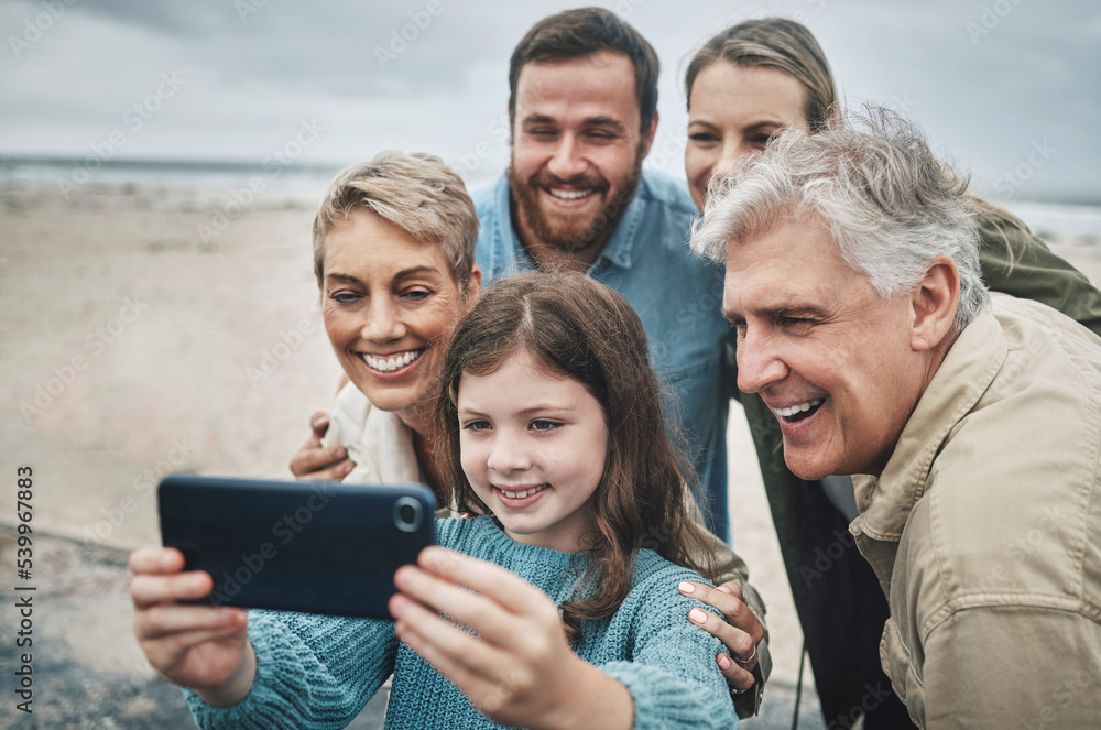 Fototapeta premium Family, selfie and girl with phone on beach for holiday, vacation or journey together by ocean. Group, mom and dad with child, grandparents and smartphone for photo in winter with smile by sea