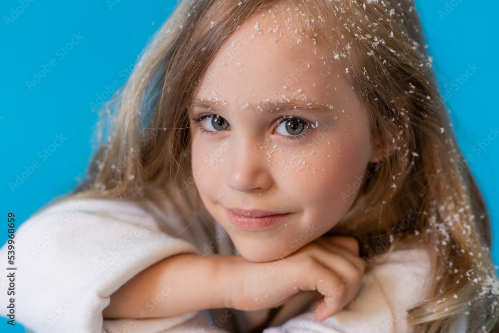 portrait of a cute little blonde girl in a white knitted sweater on a blue background in the studio. snowflakes in the hair, the concept of winter portrait of a cute little blonde girl in a white knitted sweater on a blue background in the studio. snowflakes in the hair, the concept of winter