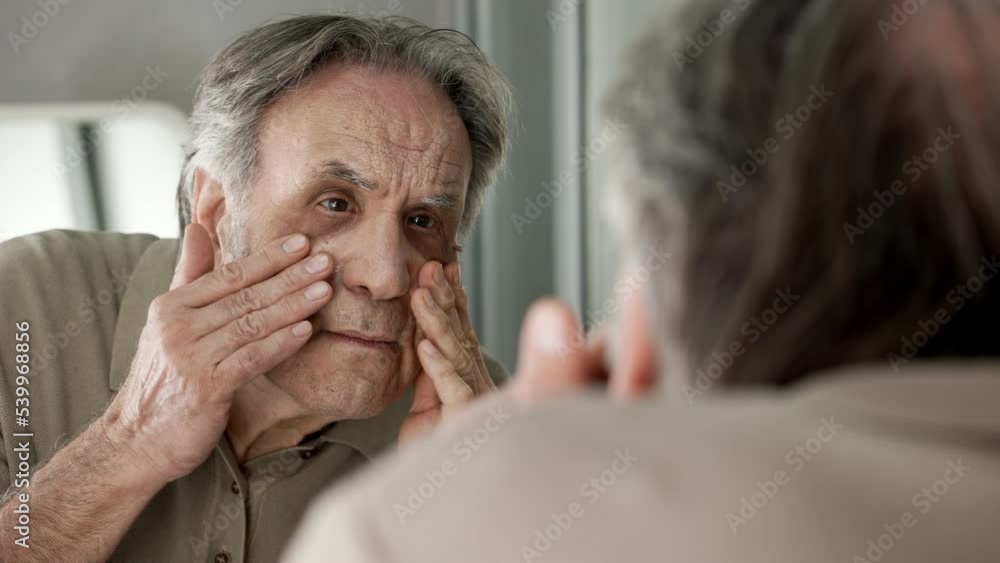 Old man examines his own eye and wrinkled in the mirror Old man examines his own eye and wrinkled in the mirror