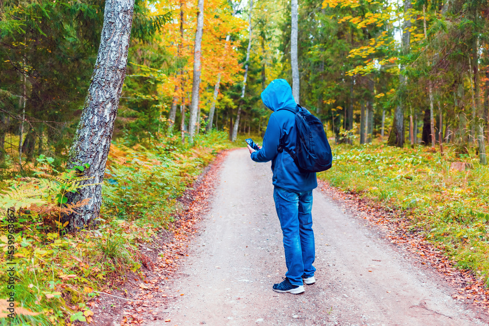 Man hiker lost in a autumn forest and search a mobile network on a hone.Tourist looking for a cellular connection on a hike.Full lenght hiker stand on the road.Travel Technology concept. Man hiker lost in a autumn forest and search a mobile network on a hone.Tourist looking for a cellular connection on a hike.Full lenght hiker stand on the road.Travel Technology concept.