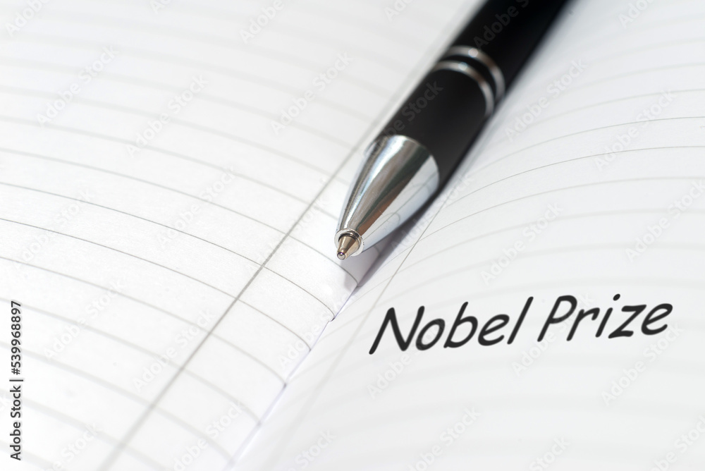 The inscription NOBEL PRIZE on a white sheet notebook.Nobel prize in literature. A pen is lying nearby.White background.Selective focus,close-up. The inscription NOBEL PRIZE on a white sheet notebook.Nobel prize in literature. A pen is lying nearby.White background.Selective focus,close-up.