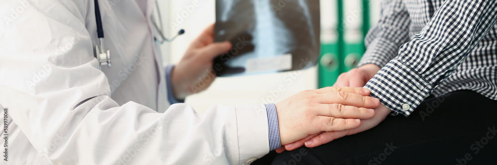 Qualified male doctor hold x ray scan of patients lungs and talk to client