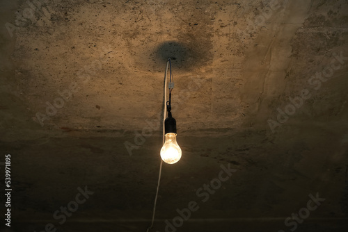 Foto Dim light bulb on grey concrete ceiling of basement or bomb shelter