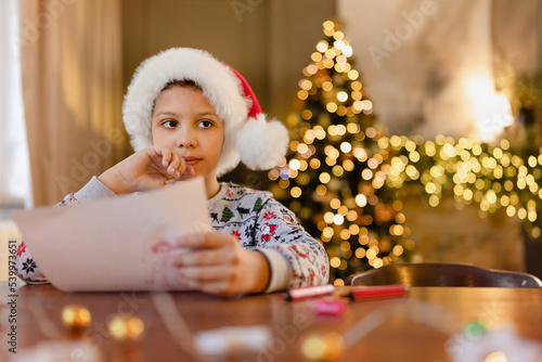 A black boy write letter for Santa near a festively decorated Christmas tree