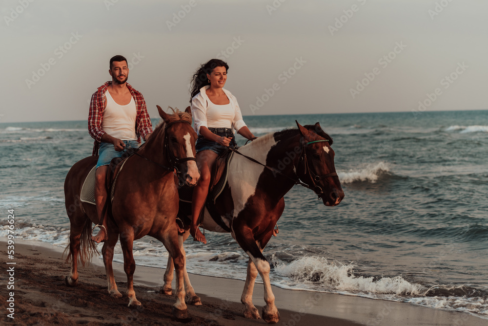 A loving couple in summer clothes riding a horse on a sandy beach at sunset. Sea and sunset in the background. Selective focus A loving couple in summer clothes riding a horse on a sandy beach at sunset. Sea and sunset in the background. Selective focus