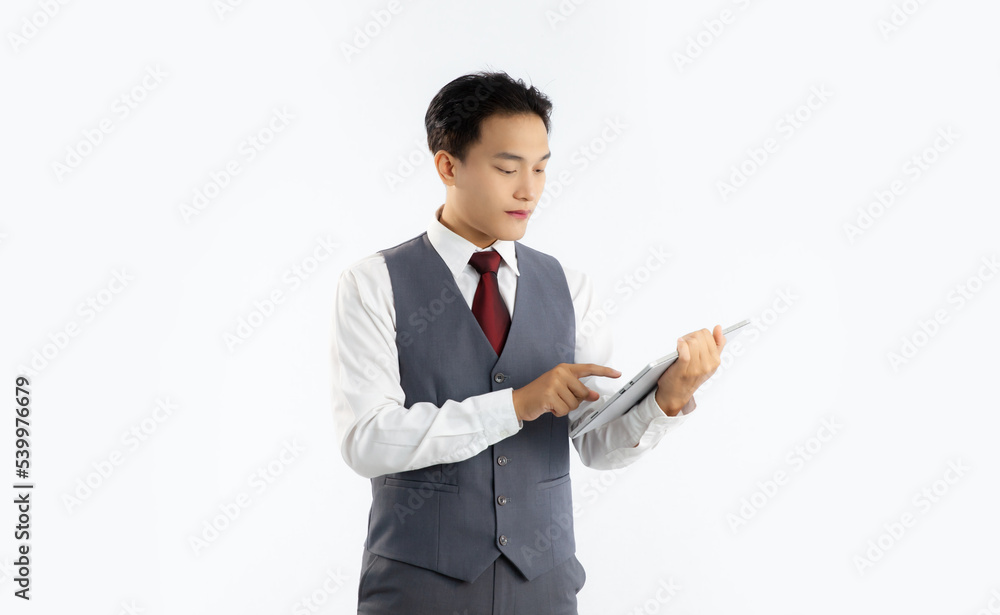 Young asian businessman in grey vest suit white shirt red tie holding tablet reading watching and touching on touchscreen white background.
Young asian businessman in grey vest suit white shirt red tie holding tablet reading watching and touching on touchscreen white background.