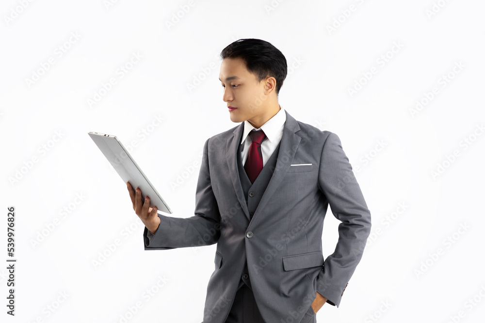 Young asian businessman in grey suit holding tablet looking and reading white background.
Young asian businessman in grey suit holding tablet looking and reading white background.