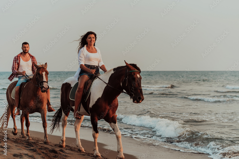 A loving couple in summer clothes riding a horse on a sandy beach at sunset. Sea and sunset in the background. Selective focus A loving couple in summer clothes riding a horse on a sandy beach at sunset. Sea and sunset in the background. Selective focus