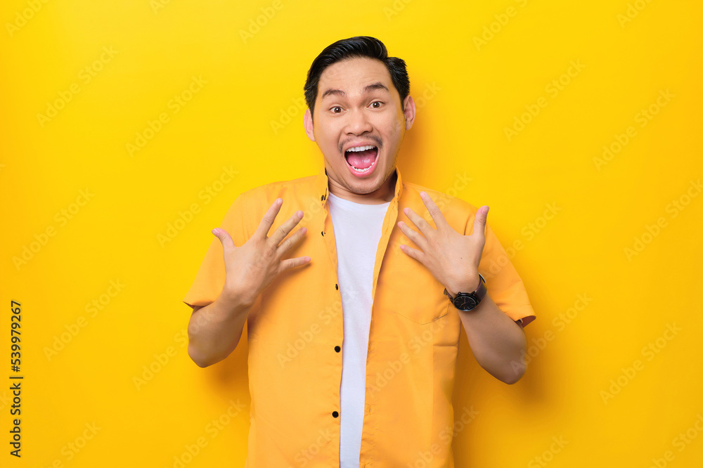 Surprised young handsome Asian man keeps hands on chest opened mouth isolated on yellow background Surprised young handsome Asian man keeps hands on chest opened mouth isolated on yellow background