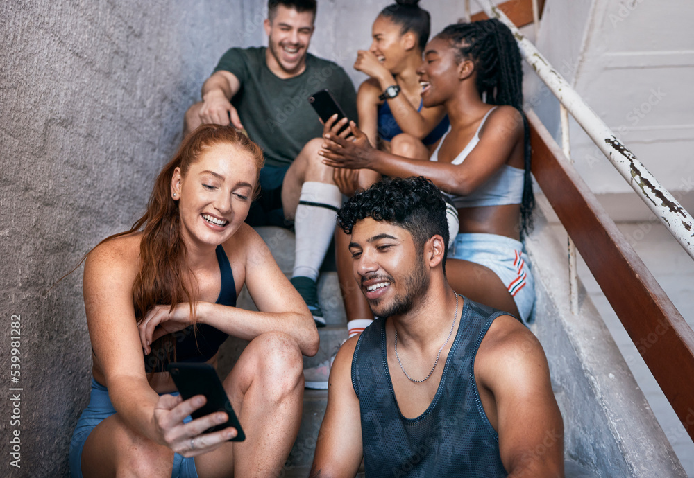 Obraz premium Fitness, phone and group of friends on stairs networking on social media together after gym workout. Happy, smile and sports people sitting and watching funny comic videos on internet with smartphone