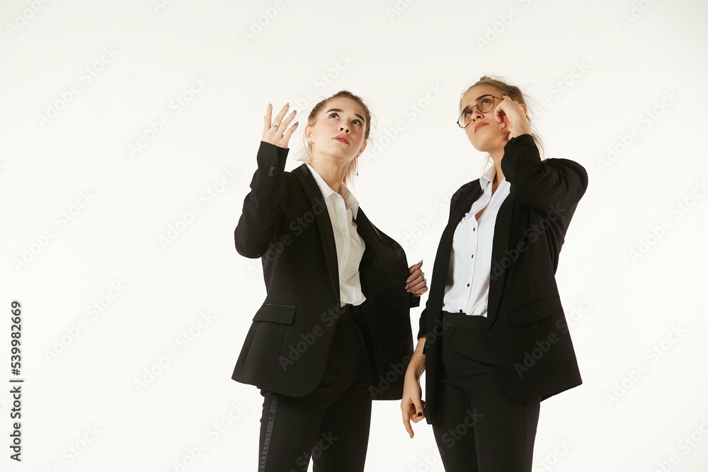 Two girls in office clothes are thinking about a project. Pure white background. The concept of business and corporate relationships in the enterprise. Two girls in office clothes are thinking about a project. Pure white background. The concept of business and corporate relationships in the enterprise.