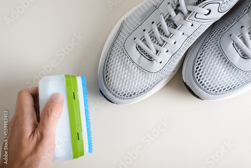 Close-up of a hand holding a cleaning sponge for shoes near sports sneakers, top view. Shoe care