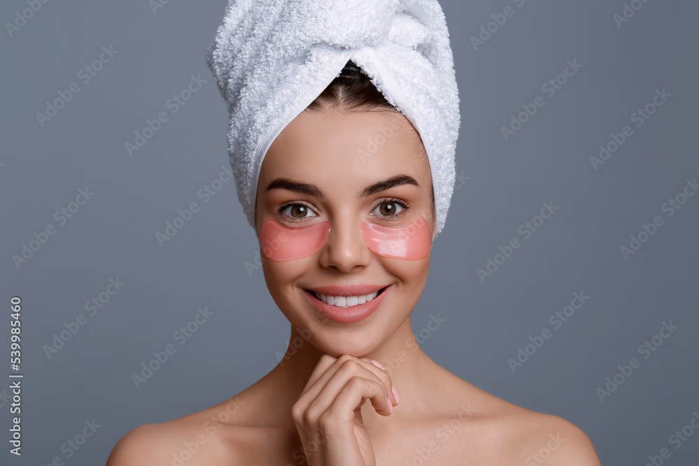 Beautiful young woman with under eye patches and hair wrapped in towel on grey background Beautiful young woman with under eye patches and hair wrapped in towel on grey background