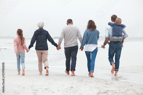Holding hands, walking and big family on the beach for exercise while on summer vacation. Grandparents, parents and children on outdoor walk in nature by ocean while on holiday, adventure or journey.