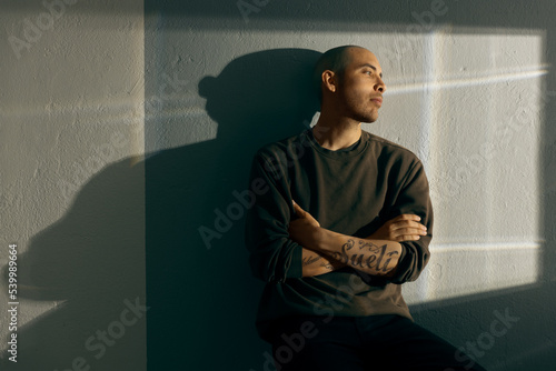 Fotografie Thoughtful portrait of a pensive man sitting with crossed arms against a textured wall