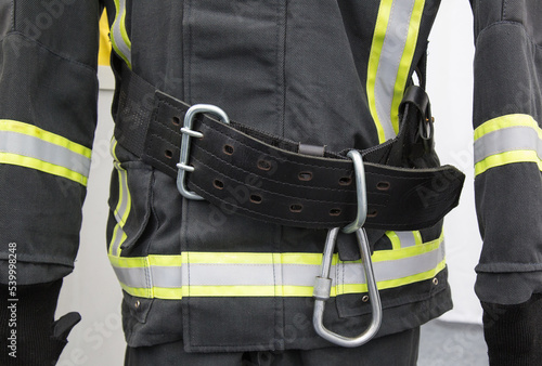 Fragment of a black protective fire suit with reflective elements and rescue belt with carabiner photo
